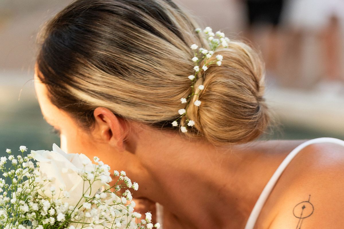 Eine Braut trägt einen eleganten Dutt mit vereinzelten weißen Blumen.