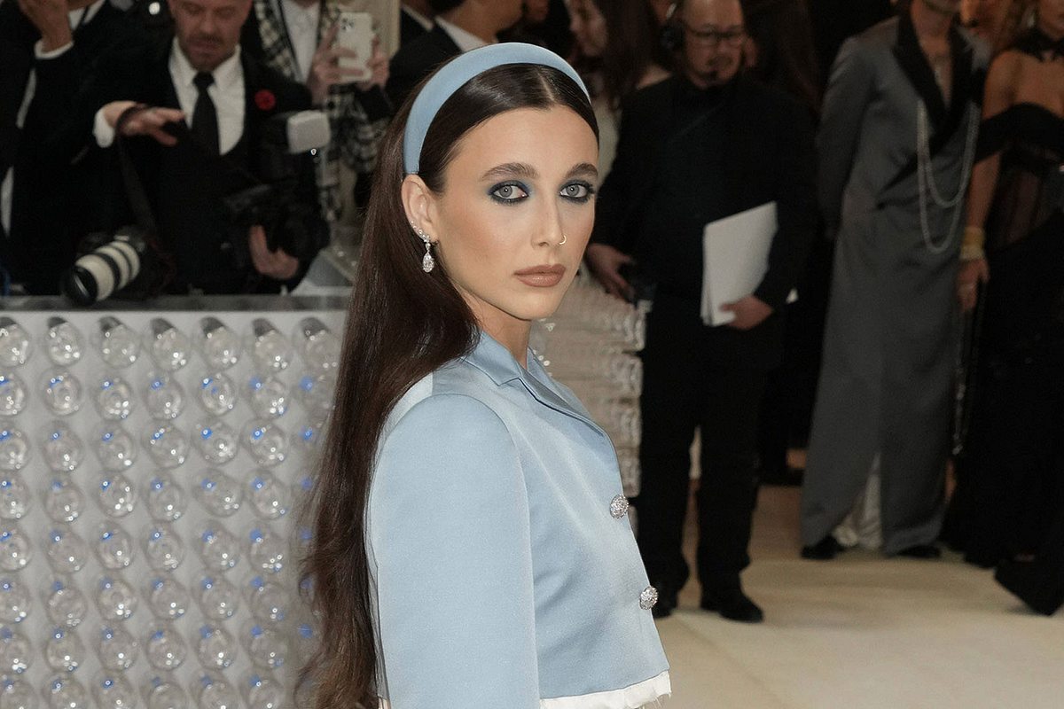 Emma Chamberlain trägt einen blauen Haarreifen passend zu ihrem blauen Outfit und lächelt für die Fotografen auf der Met Gala in die Kamera.