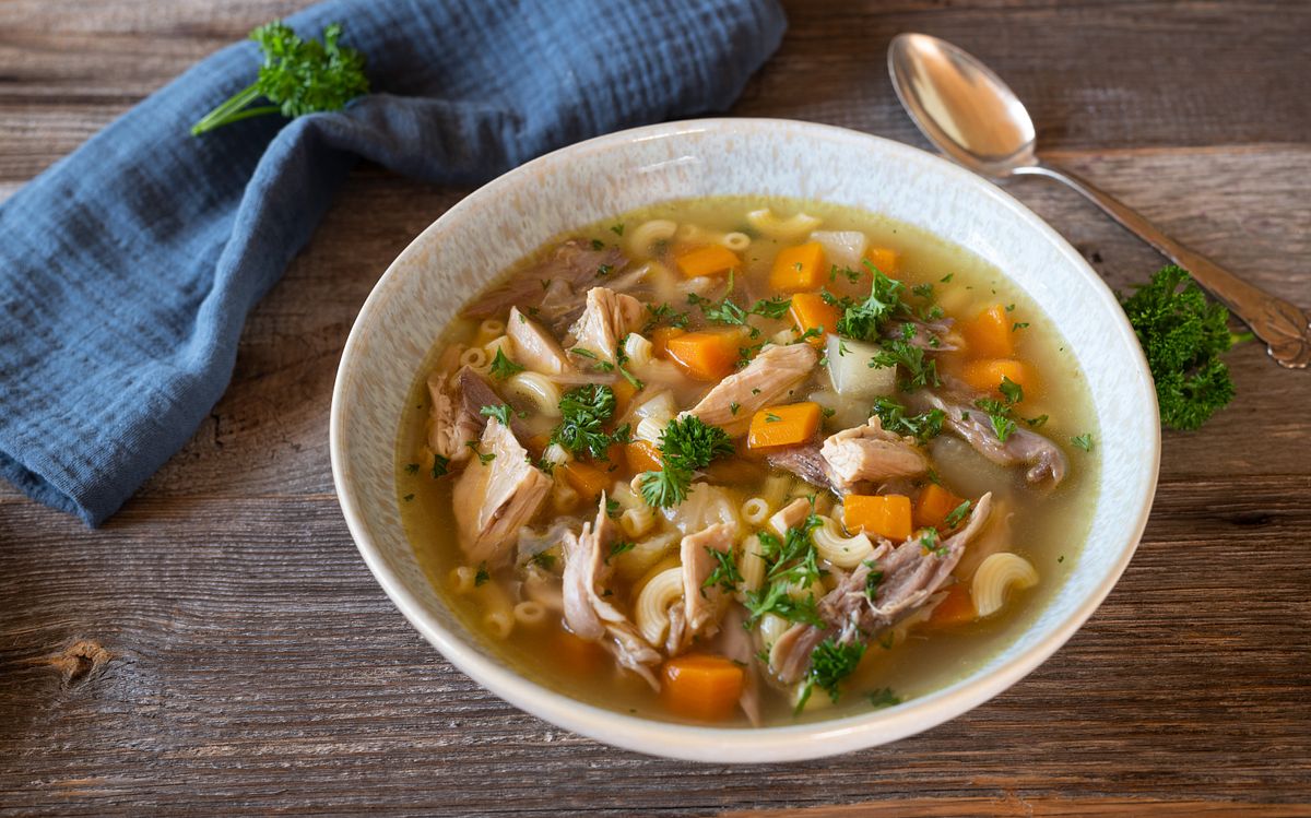 Ein Teller mit Hühnersuppe, einem Löffel und einem Lätzchen, dazu Petersiliengarnitur (Themenbild)