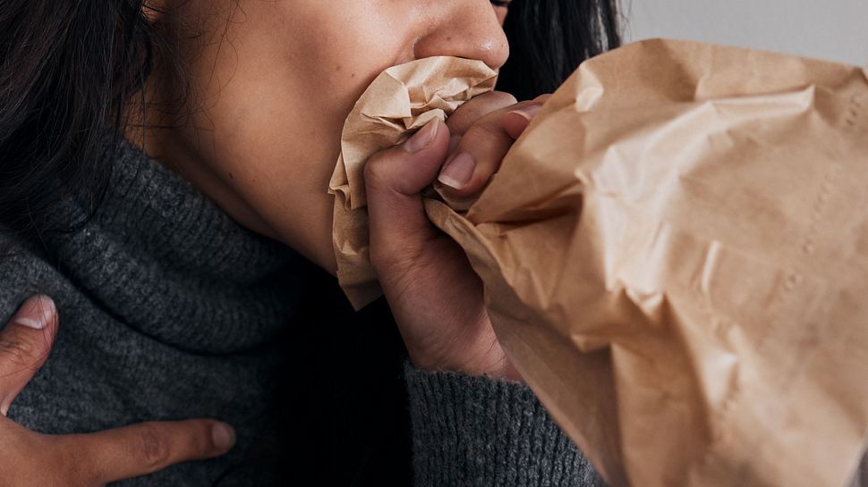 Frau, die hyperventiliert und in eine Papiertüte atmet. - Foto: PeopleImages / iStock