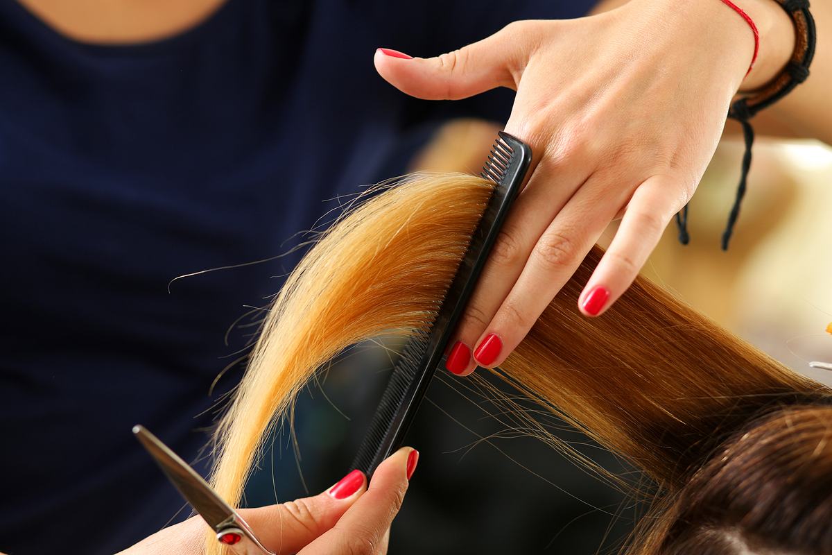 Langes blondes Haar wird beim Friseur geschnitten (Themenbild)