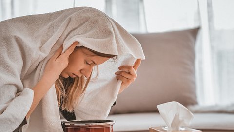 Eine Frau inhaliert eine Salzlösung mit einem Handtuch über dem Kopf (Themenbild) - Foto: ljubaphoto/iStock