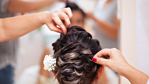 Braut von hinten mit eleganter Hochsteckfrisur und Blume im Haar, der beim fertigmachen geholfen wird  - Foto: bfk92 / iStock