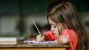 Schulmädchen schreibt konzentriert an einem Schreibtisch i ein Heft. - Foto: skynesher/iStock