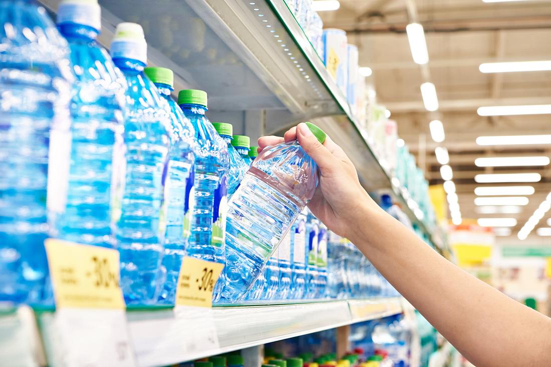 Flasche Mineralwasser von Hand aus dem Regal im Supermarkt nehmen