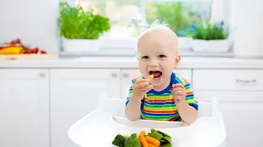 Baby das in einem Hochstuhl sitzt und Gemüse isst - Foto: iStock / FamVeld