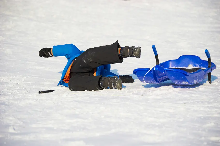 Kind liegt im Schnee, nachdem es vom Schlitten gestürzt ist