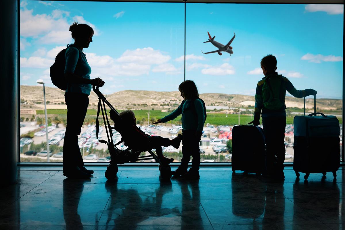Mutter mit drei Kindern und Gepäck am Flughafen bereit in die Ferien zu fliegen