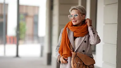 Blonde Frau mit kurzen Haaren in kariertem Wollmantel und orangenen Schal. - Foto: iStock / AnnaZhuk
