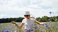Blonde Frau mit Hut und Sonnenbrille, weißem Tshirt und Rock steht in einem blühenden Feld - Foto: iStock/ Ivar Østby Simonsen Blonde Frau mit Hut und Sonnenbrille, weißem Tshirt und Rock steht in einem blühenden Feld - Foto: iStock/ Ivar Østby Simonsen