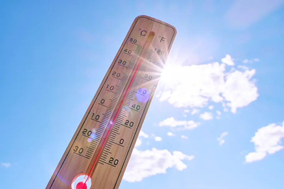 Heiße Temperaturen: Thermometer mit Sonne und blauem Himmel im Hintergrund Heiße Temperaturen: Thermometer mit Sonne und blauem Himmel im Hintergrund