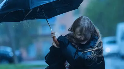 Eine Frau mit einem schwarzen Regenschirm, der vom Wind fast weg geweht wird. - Foto: iiievgeniy/iStock