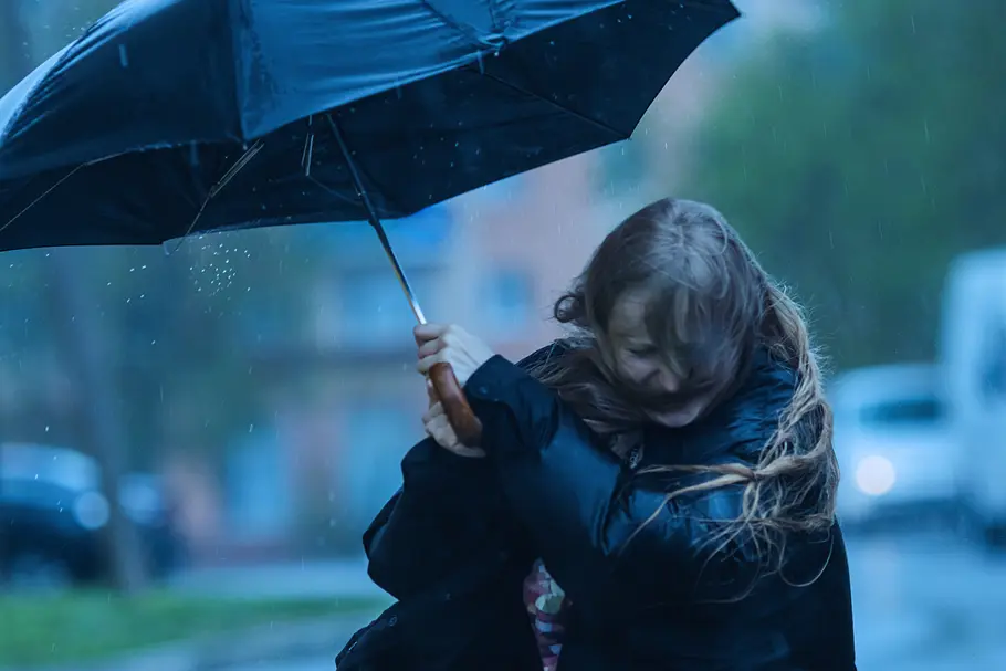 Super El Niño: Was bedeutet das Klimaphänomen für Deutschland? Eine Frau mit einem schwarzen Regenschirm, der vom Wind fast weg geweht wird.