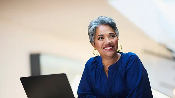 Frau mit grauen Haaren sitzt vor ihrem Laptop und trägt eine dunkelblaue Bluse - Foto: iStock/ LaylaBird