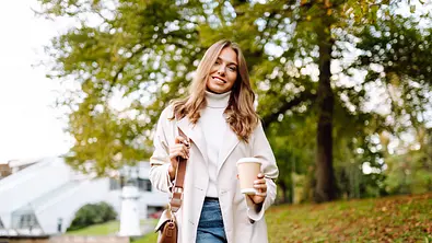 Frau mit Mantel & Kaffee in der Hand, Blick in die Kamera - Foto: iStock / Maksym Belchenko