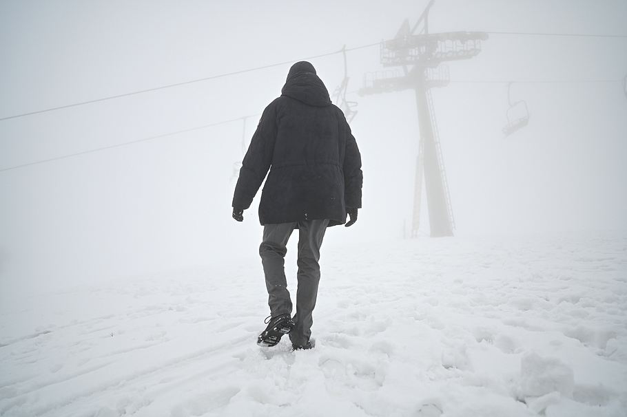 Auf dem Bild ist ein Mann in dunkler Winterkleidung von hinten zu sehen, wie er durch einen Schneesturm geht.