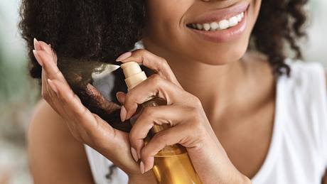 Frau sprüht Jojobaöl auf Haare - Foto: iStock/ Prostock-Studio