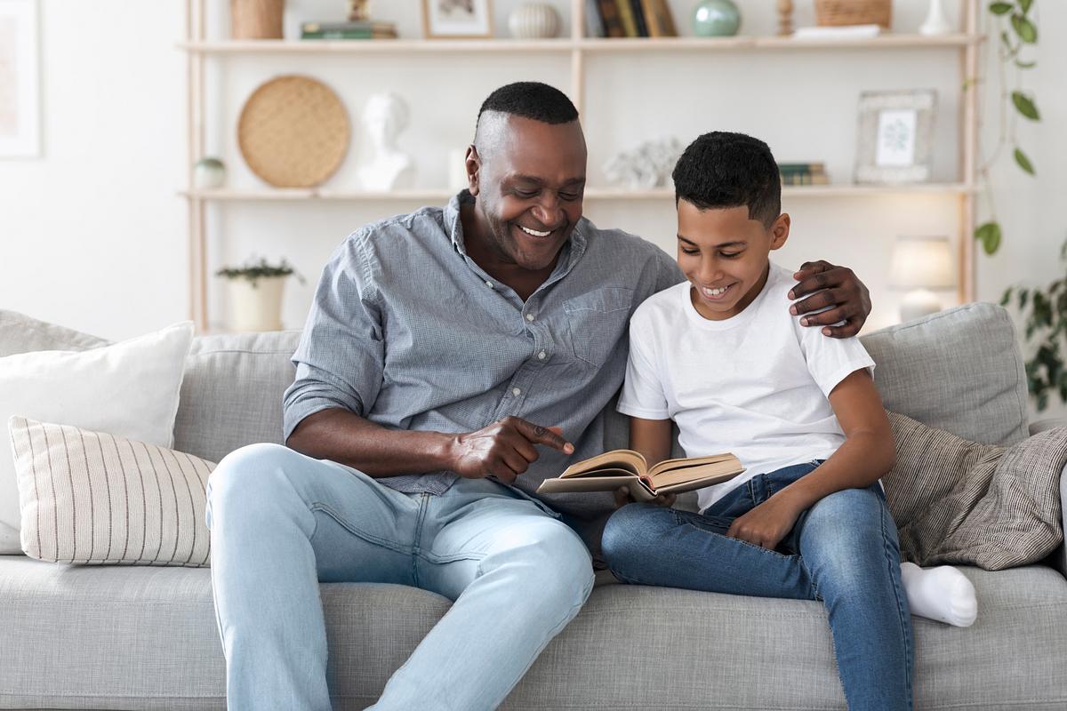 Ein Vater sitzt gemeinsam mit seinem Sohn auf einem Sofa und sie lesen gemeinsam ein Buch