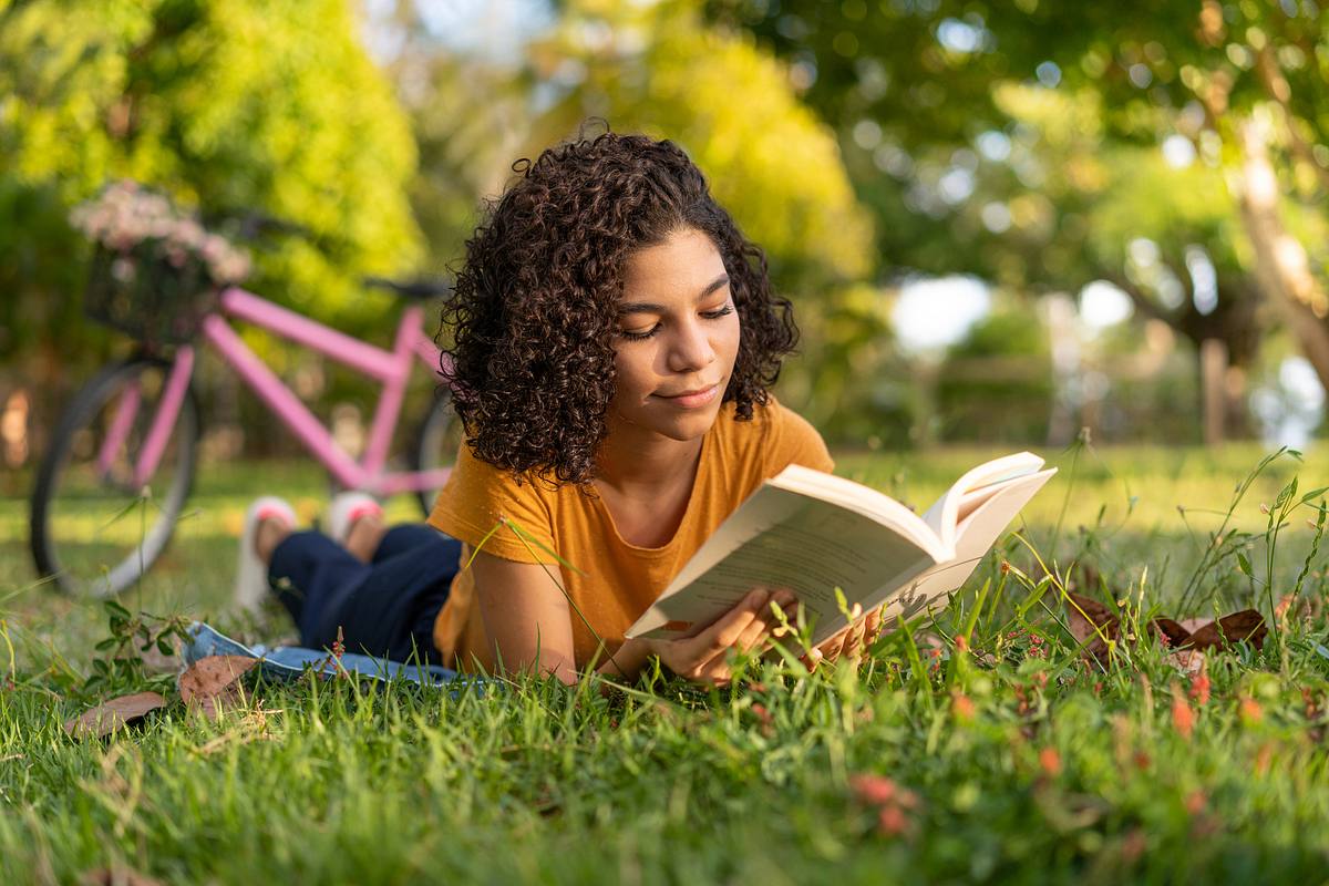 Jugendliche liest Jugendbuch Bestseller auf Wiese