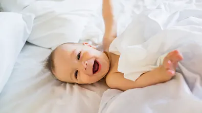 Baby liegt lachend im Bett und freut sich - Foto: iStock/ BraunS