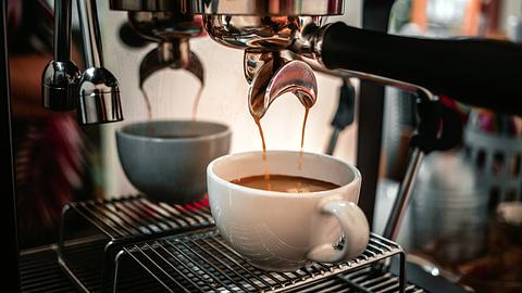 Kaffee läuft aus einem Automaten in eine weiße Tasse. - Foto: iStock / Narong KHUEANKAEW