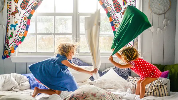 Zwei Kinder machen auf einem Bett eine Kissenschlacht.  - Foto: iStock/ Lisa5201 