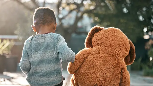 Kleines Kind sitzt mit großem Teddybären draußen in der Sonne - Foto: iStock/PeopleImages