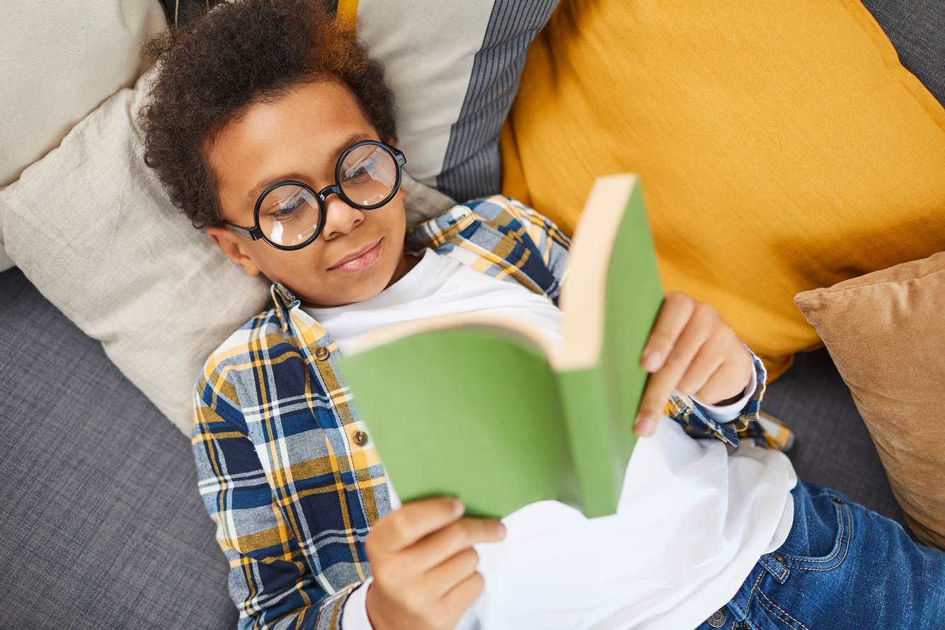 Ein Junge mit Brille liegt auf dem Sofa und liest ein Buch