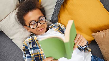 Ein Junge mit Brille liegt auf dem Sofa und liest ein Buch - Foto: iStock/SeventyFour