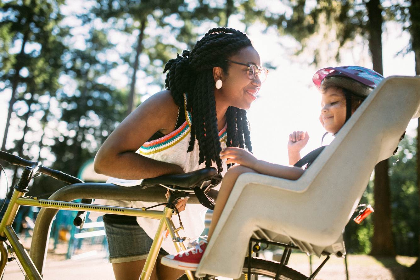 Eine Mutter lächelt ihr Kind liebevoll an, welches hinten im Fahrradsitz sitzt
