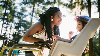 Eine Mutter lächelt ihr Kind liebevoll an, welches hinten im Fahrradsitz sitzt - Foto: iStock/RyanJLane