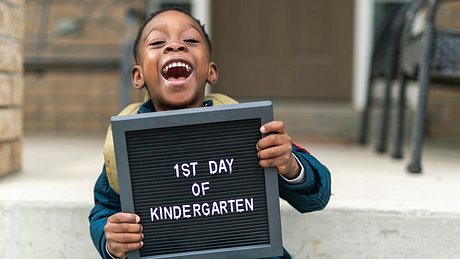 Lachender Junge mit Schild in den Händen auf dem 1st Day of Kindergarten - Foto: iStock/Fly View Productions