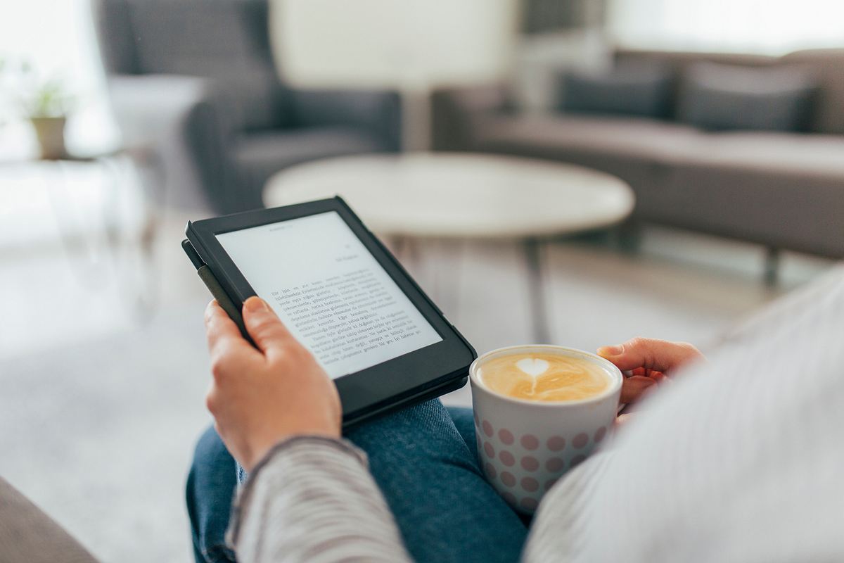 Frau sitzt auf dem Sofa und liest zu Hause ein E-Book