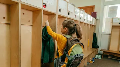 Kleines Mädchen im Vorschulalter hängt ihre Jacke an eine leere Kita-Gaderobe - Foto: i-Stock/lithiumcloud