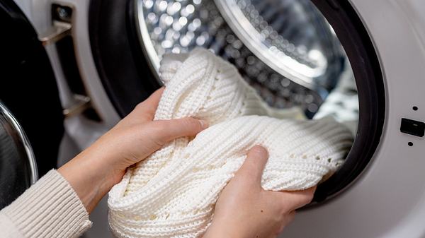 Frau steckt weißen Pullover in die Trommel einer Waschmaschine - Foto: Damian Lugowski/ iStock