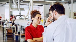 Chef redet auf müde aussehende Angestellte ein und gibt ihr mit einer Geste zu verstehen, dass er sie im Auge behält. - Foto: dusanpetkovic / iStock