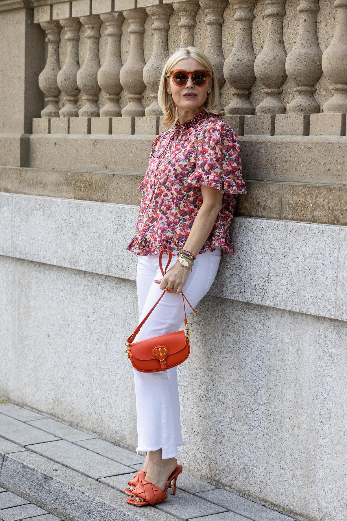 Lässig-elegante Kombination: Weiße Jeans mit bunt gemusterter Bluse, in der Rot-Töne dominieren. Auch die Accessoires und Schuhe sind in Rot gehalten.