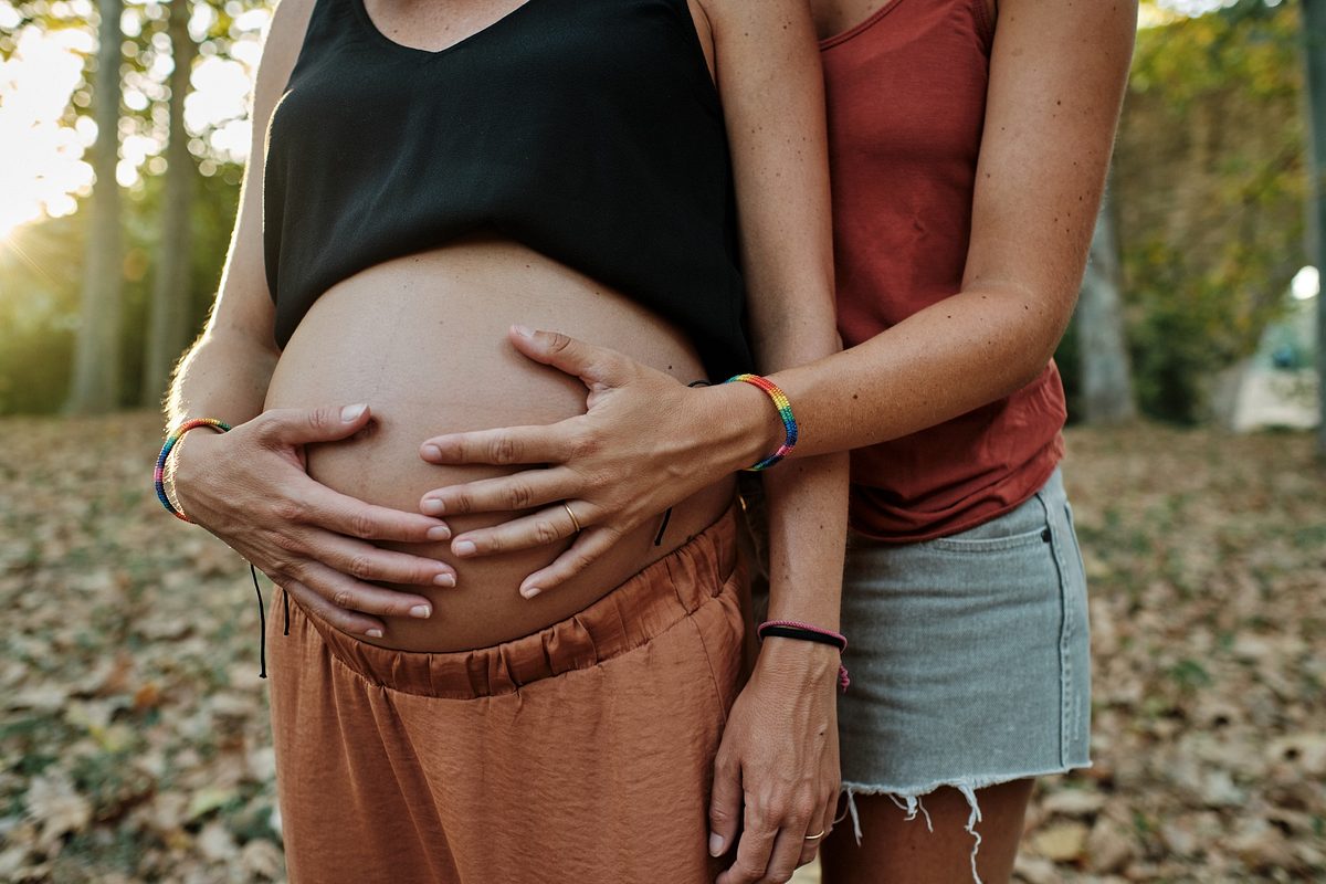 Nahaufnahme eines lesbischen Paares, das ihren Schwangerschaftsbauch in einem Park hält