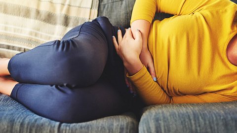 Frau liegt mit Schmerzen in der Magengegend auf dem Sofa (Themenbild) - Foto: Charday Penn/iStock