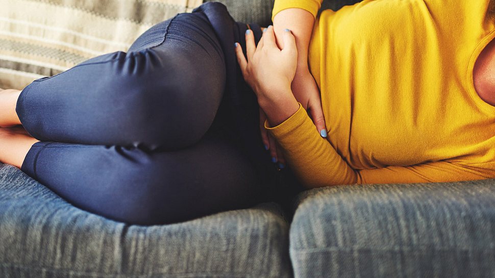 Frau liegt mit Schmerzen in der Magengegend auf dem Sofa (Themenbild) - Foto: Charday Penn/iStock