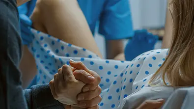 Mann hält die Hand einer Frau, die ein Kind zur Welt bringt. - Foto: gorodenkoff/iStock