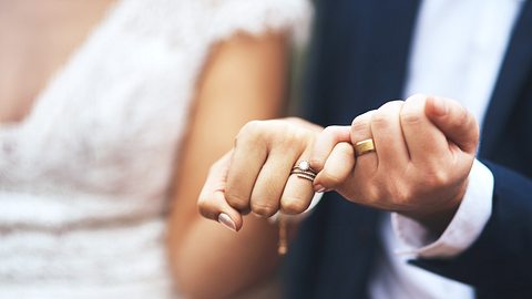 Nahaufnahme Brautpaar, hält einander die kleinen Finger. - Foto: PeopleImages / iStock