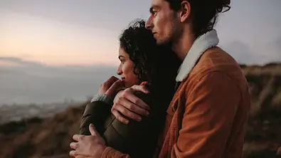 Ein junges Paar steht an einem Strand im Frühling und umarmt sich. - Foto: jacoblund/iStock