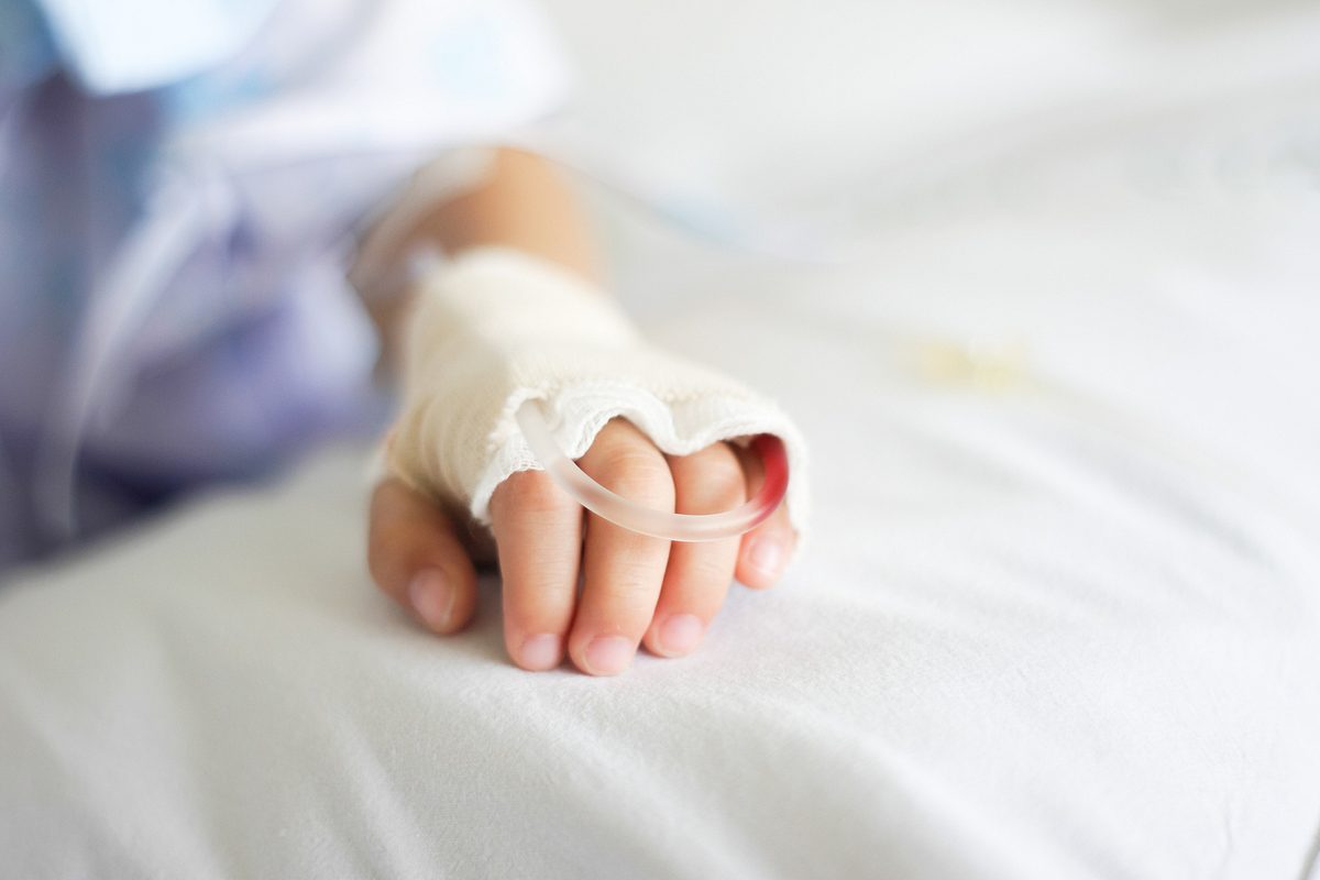 Hand eines Kindes mit Schlauch auf Krankenhausbett.
