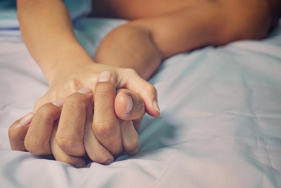 Nahaufnahme von ineinander verschränkten Händen von Mann und Frau auf einem Bett.