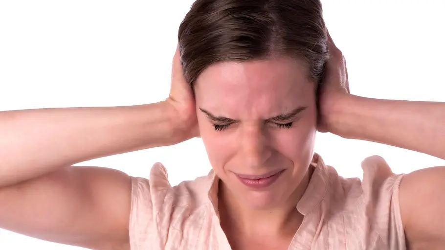 Misophonie. Eine Frau hält sich mit beiden Händen die Ohren zu und hat ein schmerzverzerrtes Gesicht.