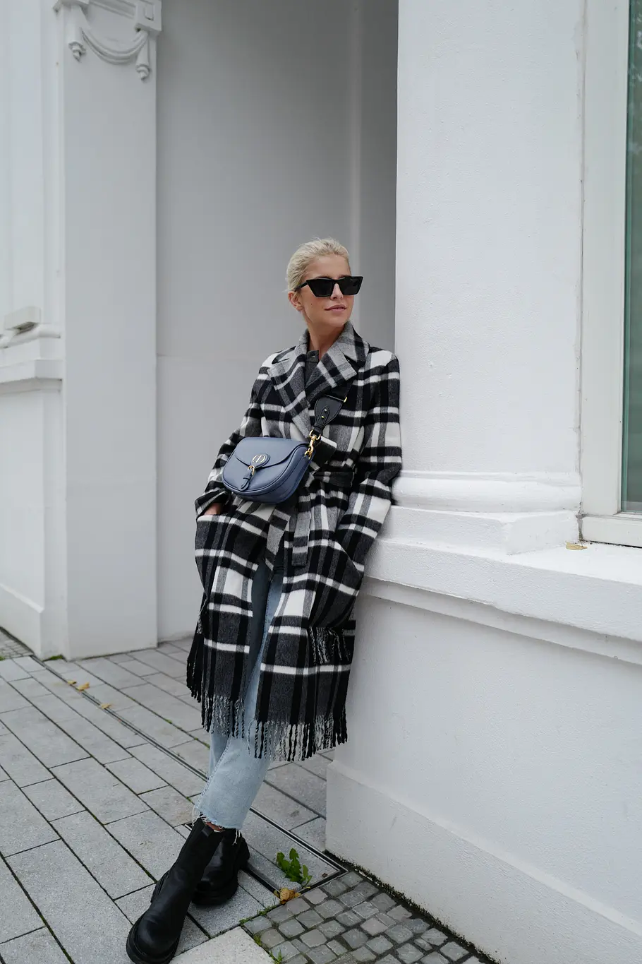 Mom Jean Outfit Winter Kombis mit Must-Have Potenzial Frau mit Karo-Mantel, Chealsea Boots und blauer Handtasche