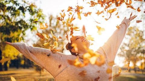 Frau wirft herbstliche Blätter in die Luft - Foto: iStock/urbazon