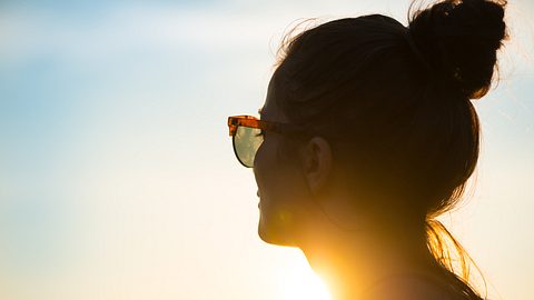 Frau mit Sonnenbrille vor Sonnenuntergang - Foto: iStock/Warchi