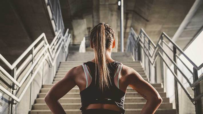 Frau in Sportoutfit steht vor Treppe und hat die Hände in die Hüften gestemmt (Themenbild) - Foto: jelenahinic/iStock (Themenbild)